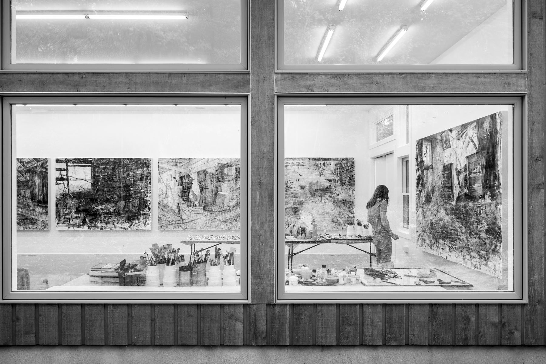 Damian Stamer at work in his studio, seen through the studio windows: large paintings on the walls, a table of brushes and paint.